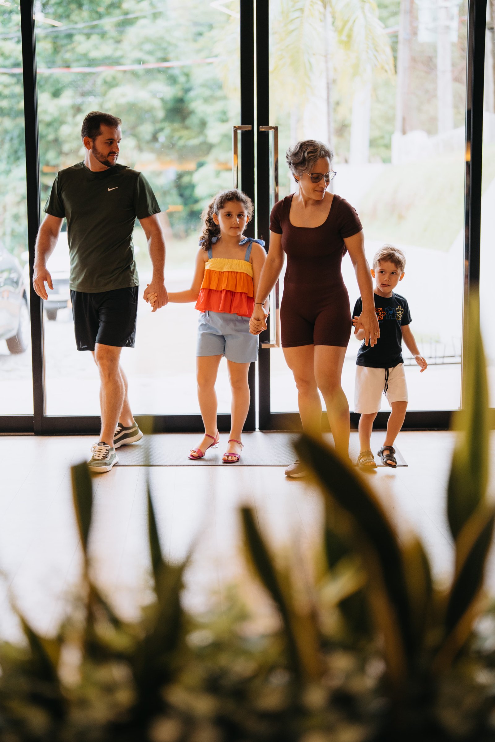 Família entrando na Monin Academia: pai, mãe e duas crianças caminhando juntos pela entrada